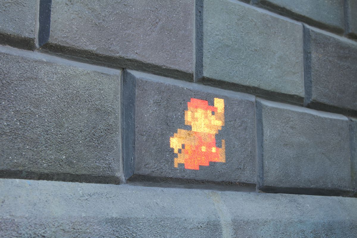 A projection of pixelated Mario against a brick wall backdrop.