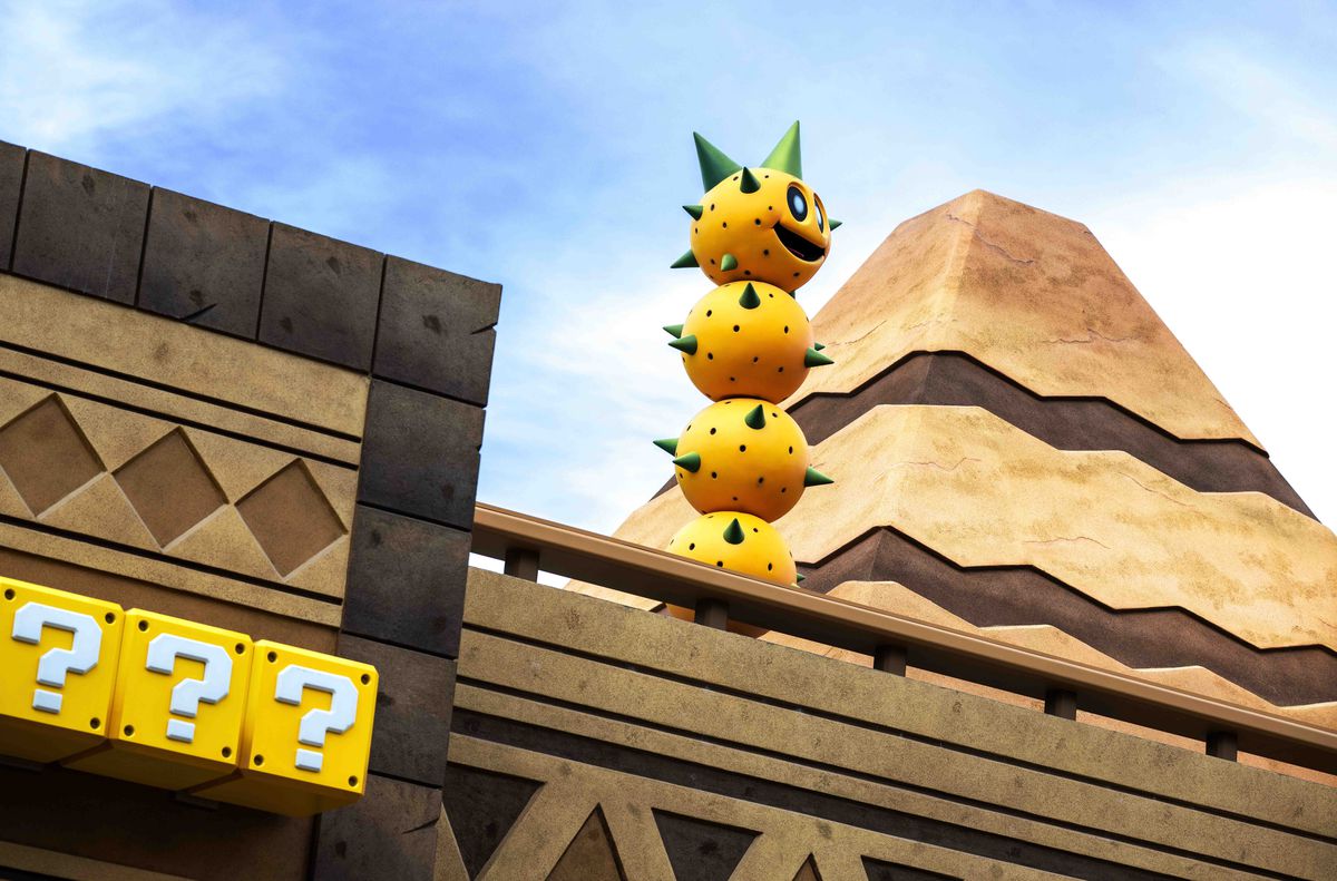 A photo from Super Nintendo World, with a tall Pokey in front of a pyramid, and coin blocks in the foreground.